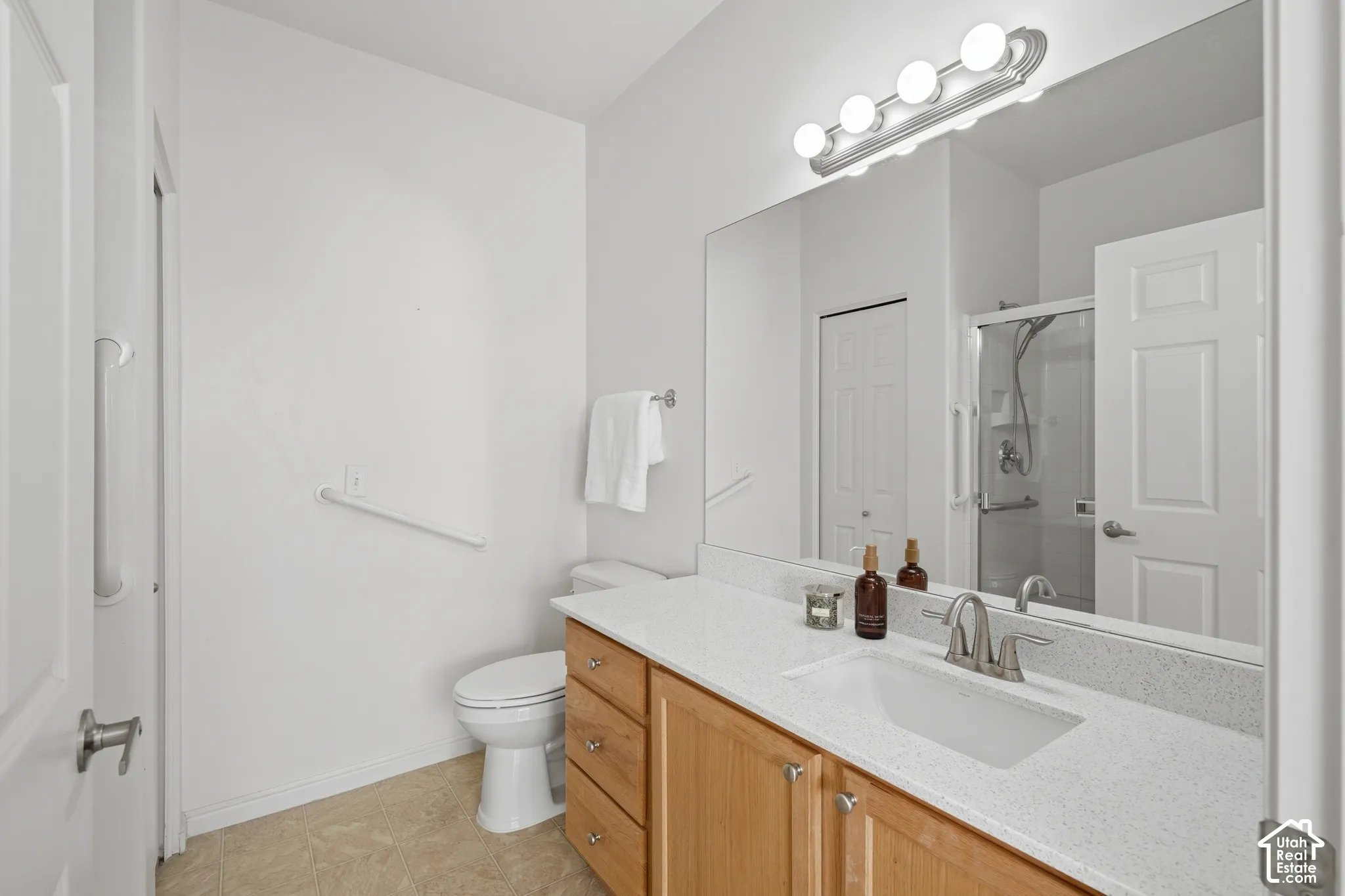 Bathroom featuring a vanity with light-tone wood cabinetry, a solid surface countertop with an integrated rectangular sink, a full-width wall mirror, and an overhead four-bulb fixture