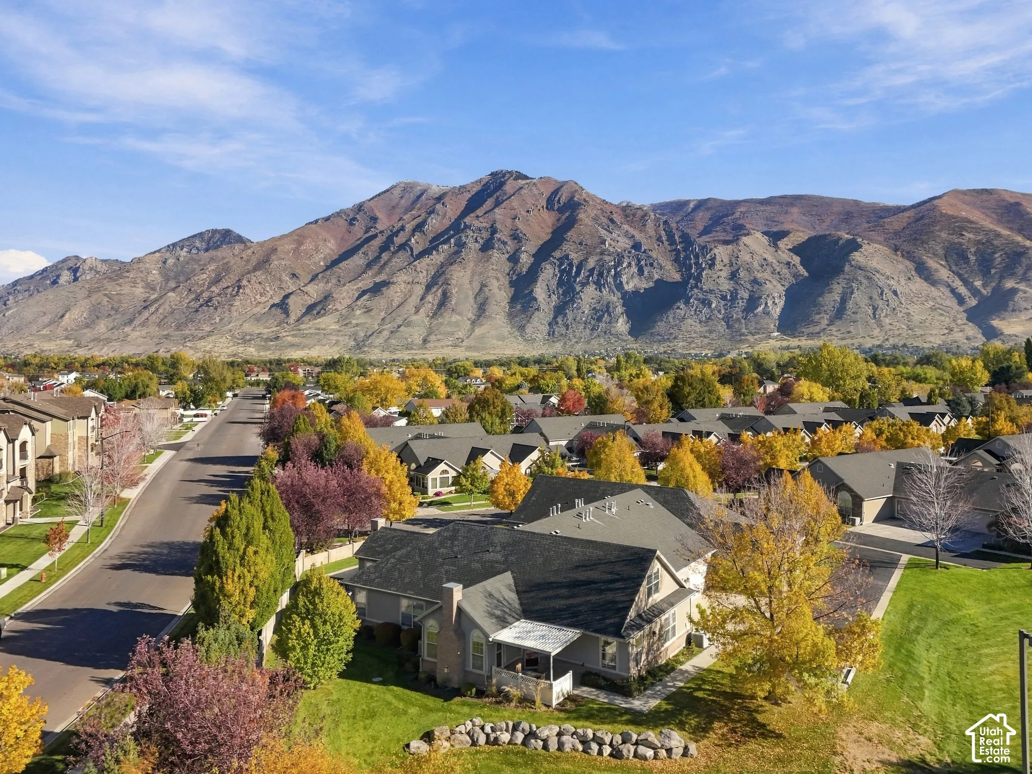 Aerial perspective featuring a multi-gabled residence with a stone and siding exterior, expansive lawn, stone hardscaping, and a prominent mountain backdrop