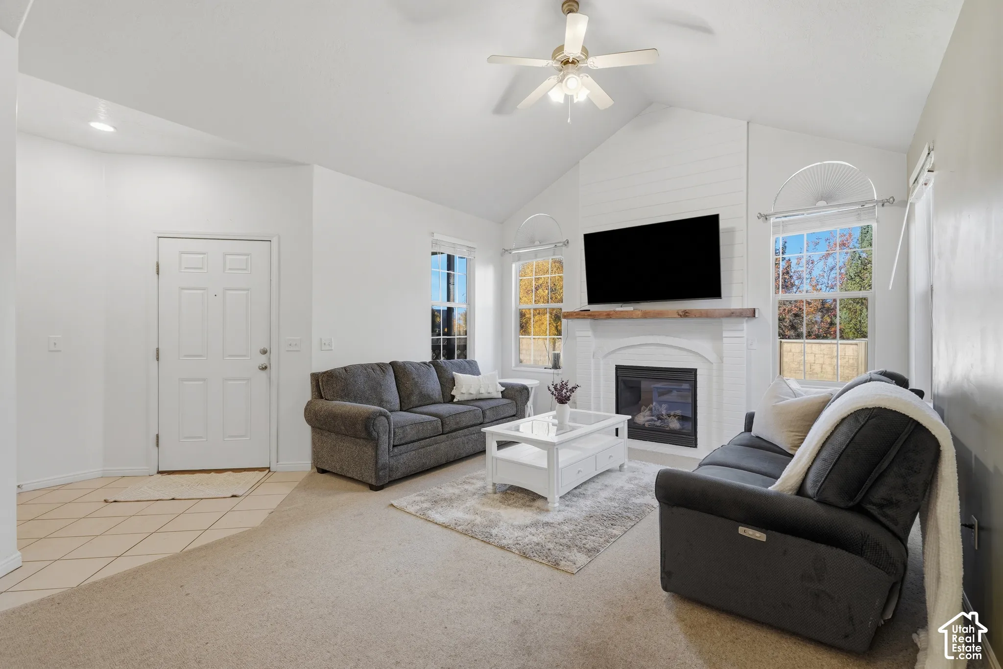 Vaulted ceilings, fireplace with a painted brick surround, custom wood mantel, ceiling fan, and multi-pane windows