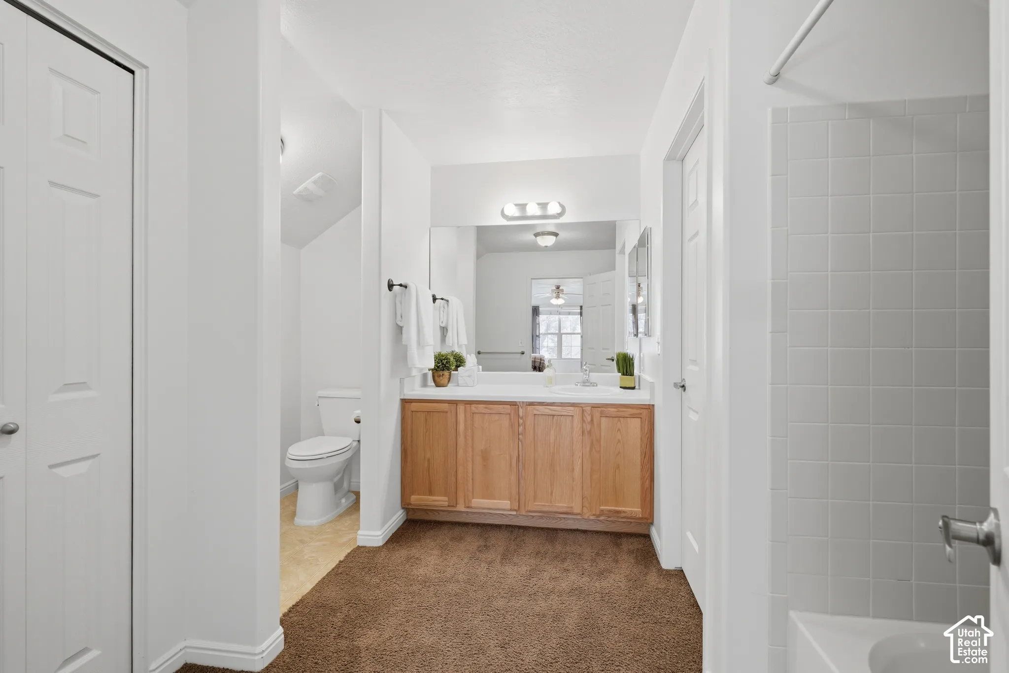 Bathroom featuring a vanity with light-wood cabinetry, a full-width wall mirror, a three-bulb vanity light fixture, and a tiled shower surround