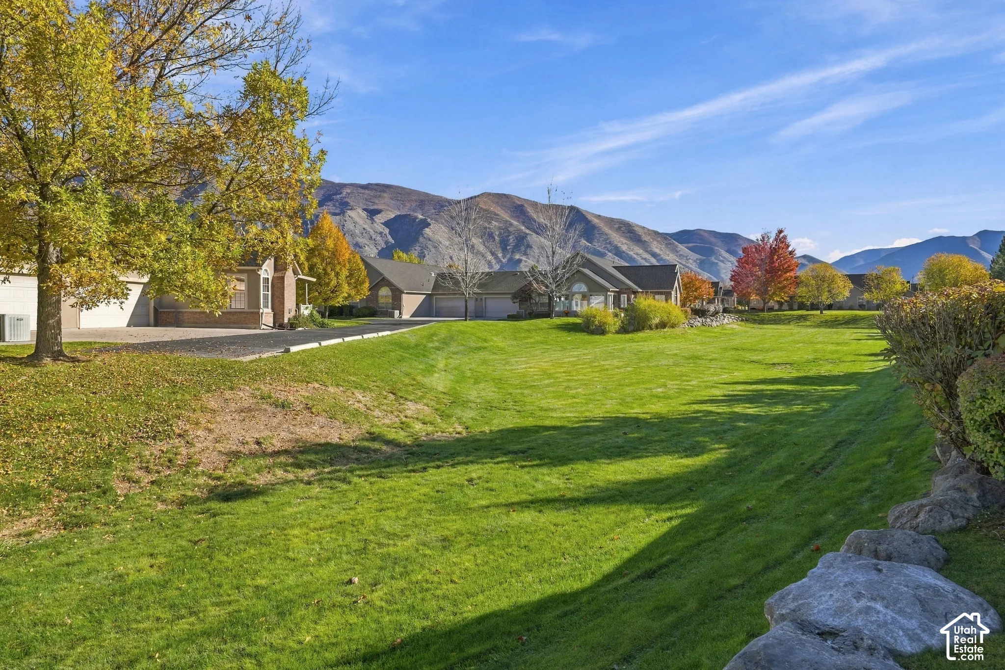 Expansive lawn area featuring mature trees, natural stone retaining walls, and a mountain backdrop