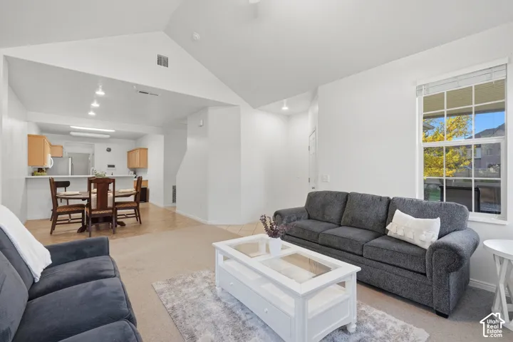 Vaulted ceilings, neutral wall palette, single-hung window with muntins, recessed lighting, and kitchen bar seating
