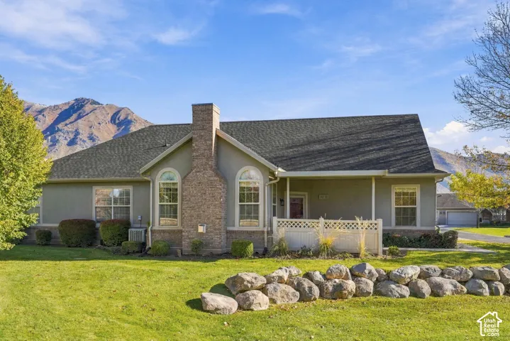 Single-story residence featuring a partial stone facade, prominent chimney, covered front porch with lattice railing, and mountain backdrop