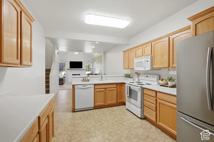 Kitchen featuring light wood cabinetry, white countertops, integrated white appliances, a stainless steel refrigerator, and resilient sheet flooring
