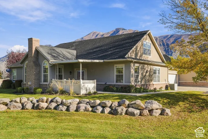 Exterior featuring a natural stone retaining wall, brick and stucco facade, covered porch with lattice railing, and a mountain backdrop