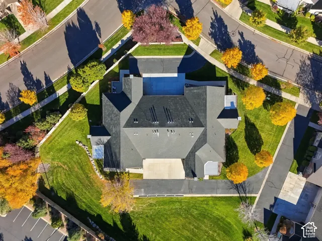 Aerial perspective of a corner lot property featuring a multi-gabled asphalt shingle roof, expansive manicured lawn, mature deciduous trees, and paved driveway