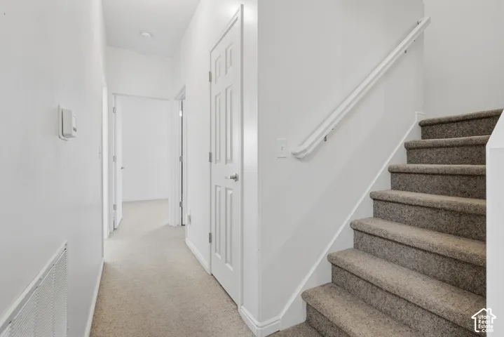 Staircase featuring neutral carpeting and a white handrail, complemented by interior doors and light-toned carpeted flooring