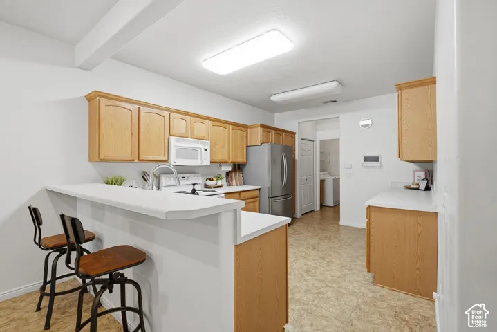 Kitchen featuring light wood cabinetry, white countertops, a breakfast bar, stainless steel refrigerator, and integrated over-the-range microwave