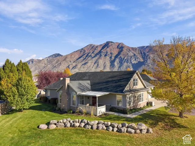 Single-story residence featuring a brick and siding exterior, covered front porch, stone retaining wall, and mountain backdrop