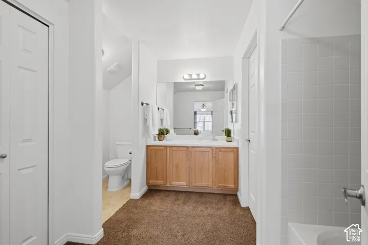 Bathroom featuring a vanity with light-wood cabinetry, a full-width wall mirror, a three-bulb vanity light fixture, and a tiled shower surround