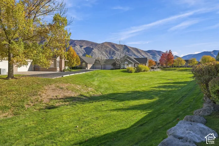 Expansive lawn area featuring mature trees, natural stone retaining walls, and a mountain backdrop