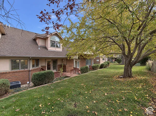 Rear exterior featuring a brick and stucco facade, an arched window dormer, wood decking, and mature landscaping