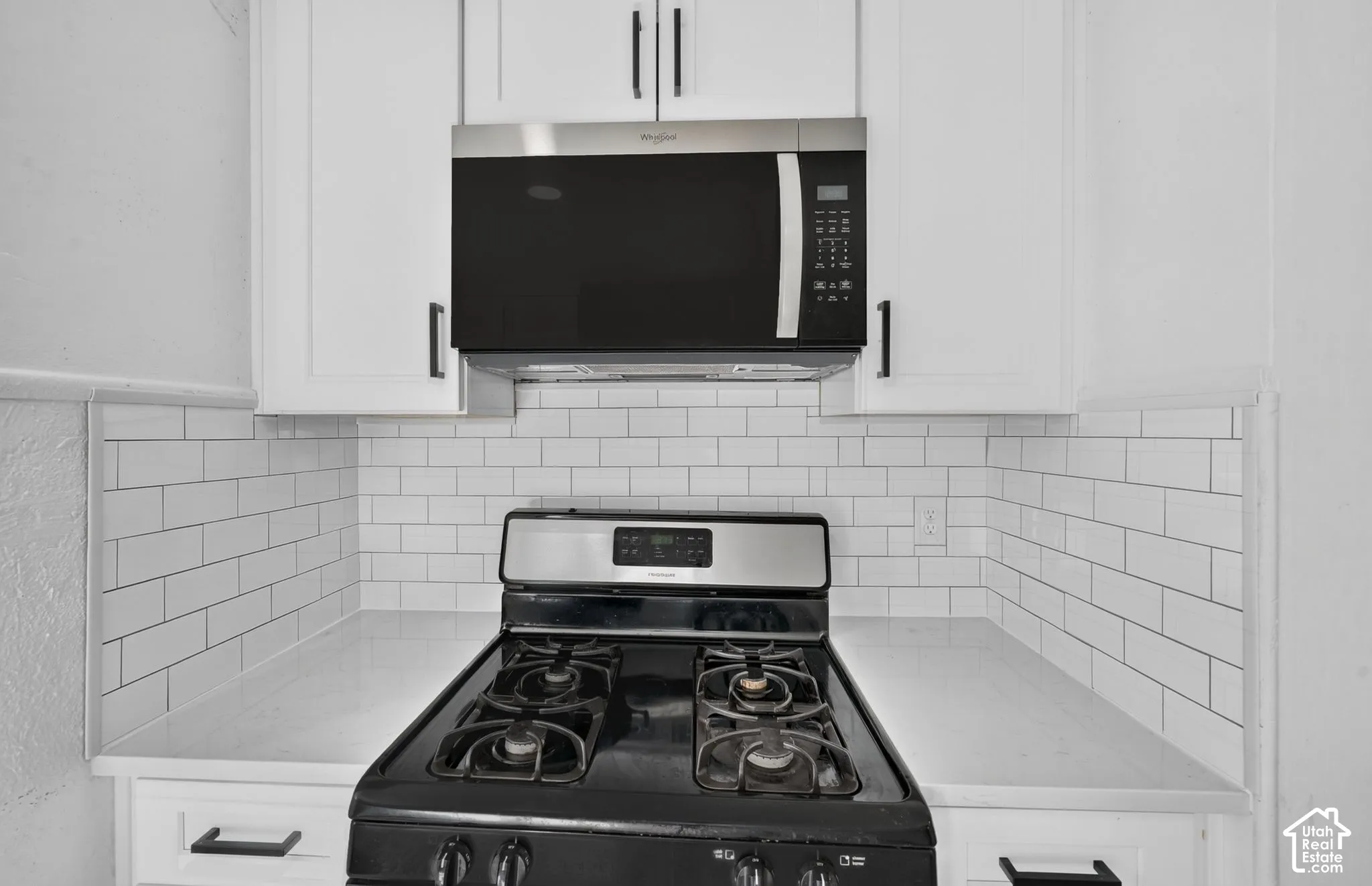 White shaker-style cabinetry with matte black hardware, subway tile backsplash, solid-surface countertops, and stainless steel built-in microwave and gas range