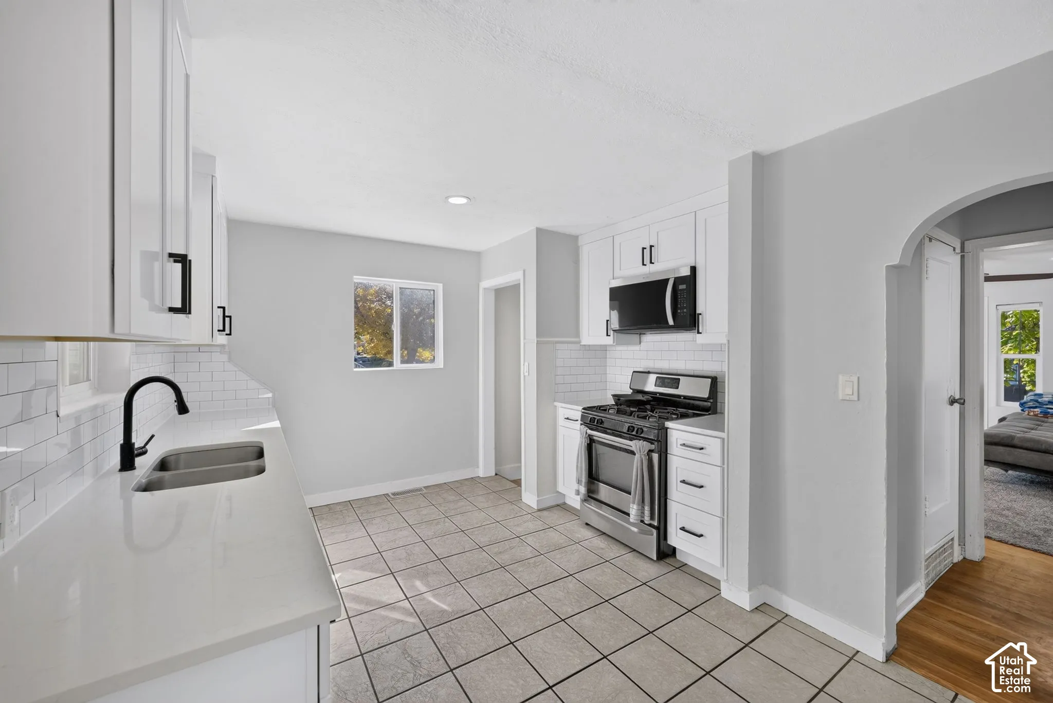 Kitchen featuring white cabinetry, quartz countertops, subway tile backsplash, stainless steel appliances, and tile flooring