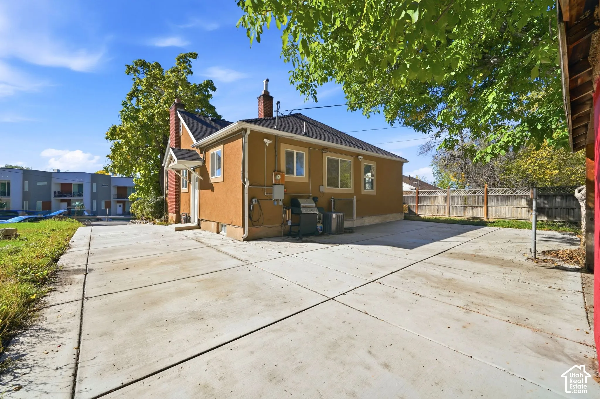 Stucco exterior featuring a dual-chimney roofline, large concrete parking area, and wood-panel fencing