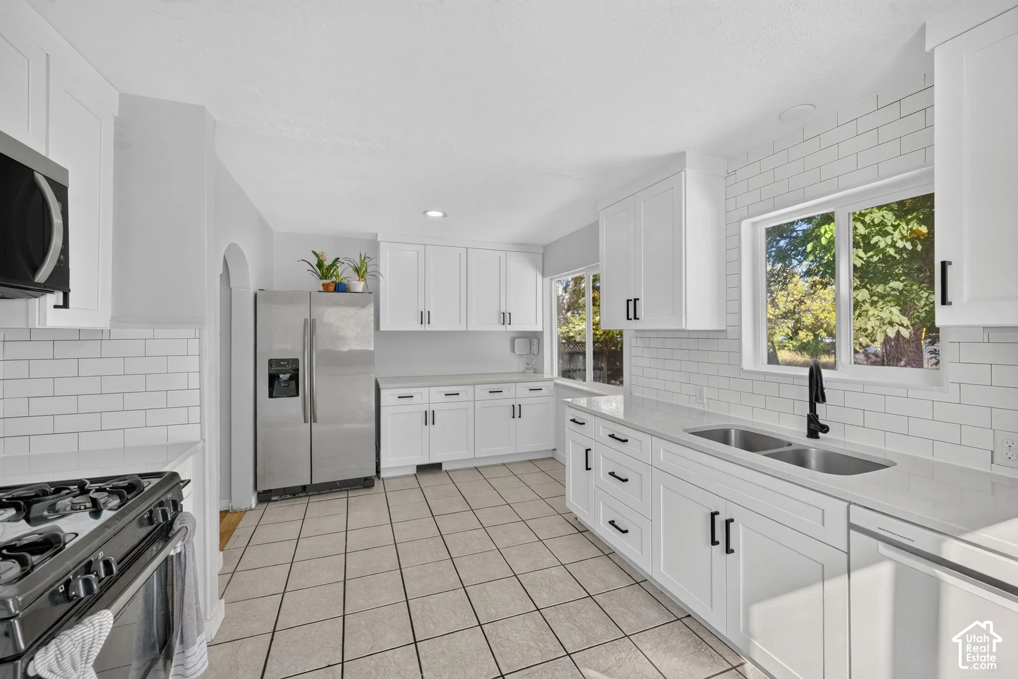 Kitchen featuring white cabinetry with matte black hardware, stone-finish countertops, white subway tile backsplash, and ceramic tile flooring