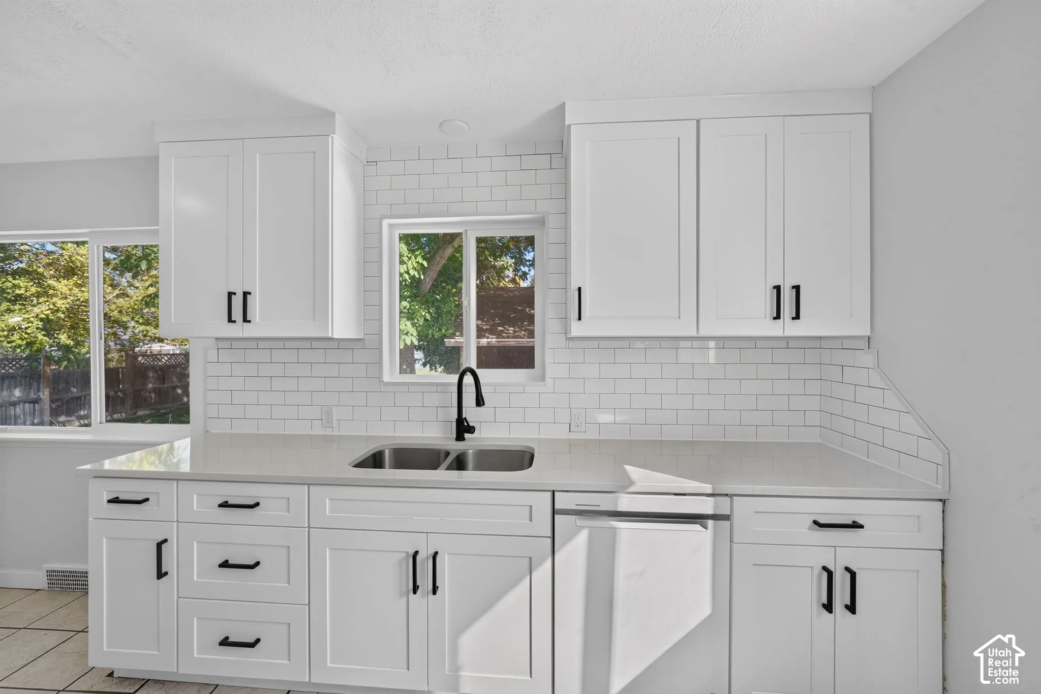 Kitchen featuring white shaker-style cabinetry, matte black hardware, quartz countertops, a white subway tile backsplash, and an undermount double-basin stainless steel sink with a matte black faucet