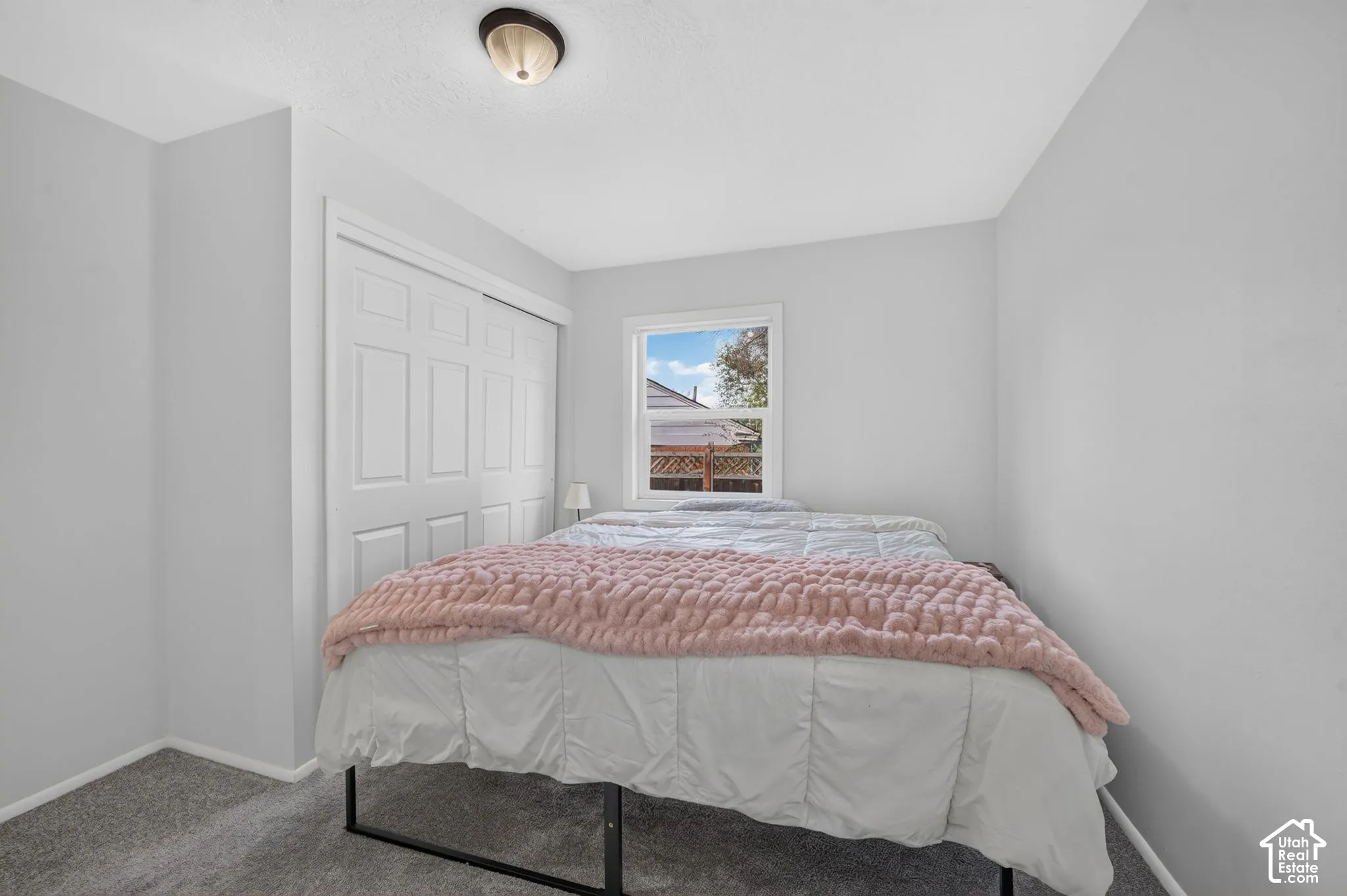 Neutral-toned interior featuring wall-to-wall carpeting, a multi-panel closet door, a single-hung window with white trim, and a semi-flush mount ceiling light fixture