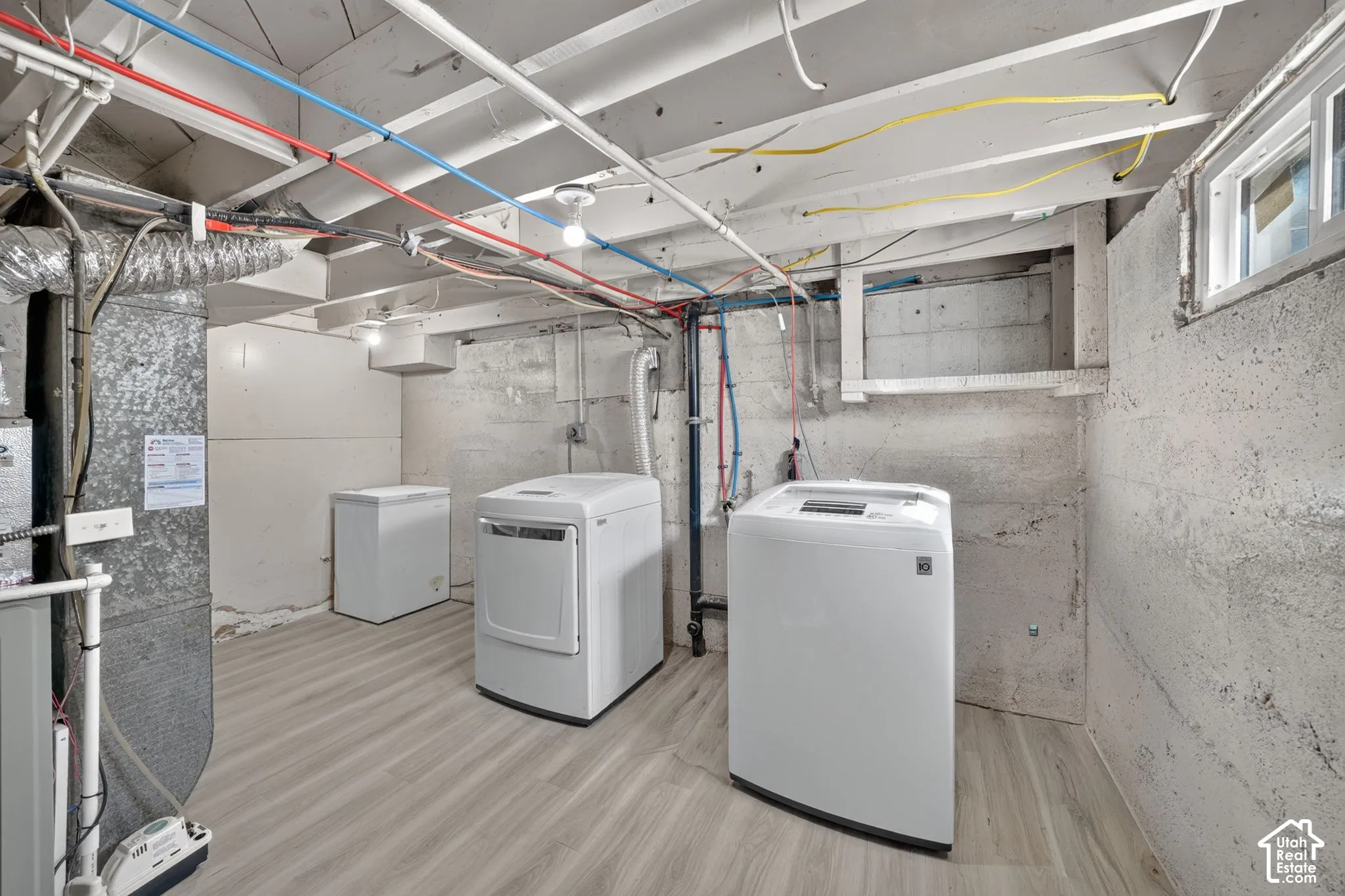 Utility area featuring exposed ceiling joists, light-tone wood-finish flooring, and concrete block wall construction