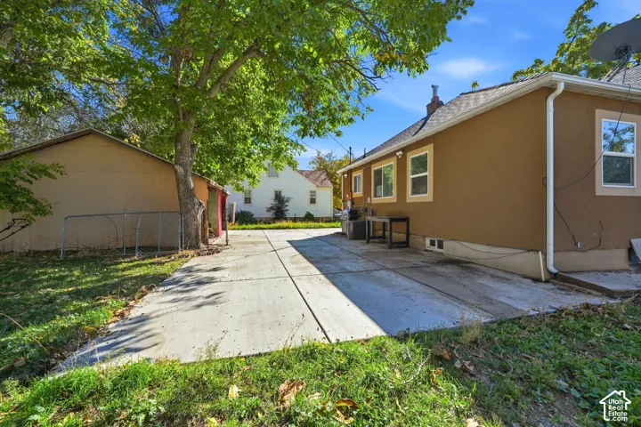 Stucco exterior featuring a concrete driveway, detached structure, and mature trees