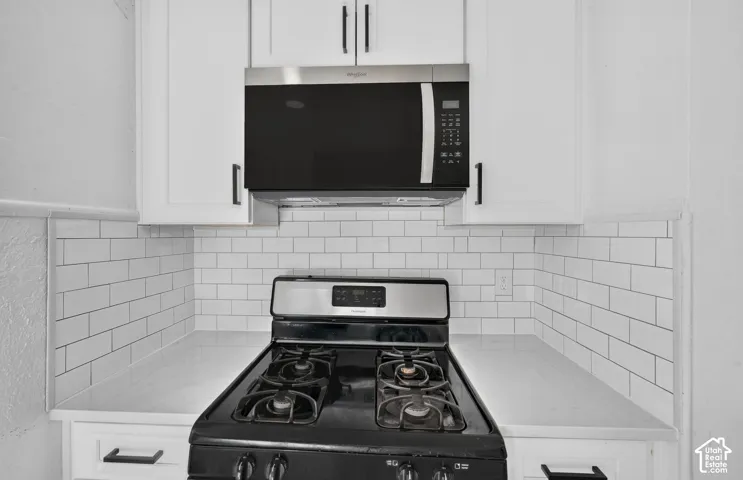 White shaker-style cabinetry with matte black hardware, subway tile backsplash, solid-surface countertops, and stainless steel built-in microwave and gas range