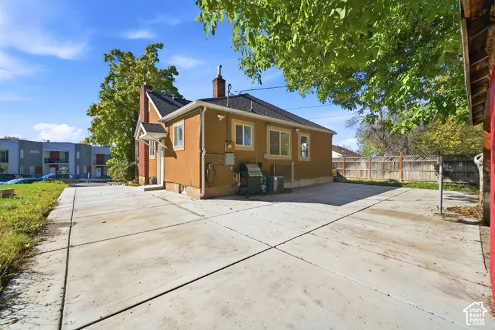 Stucco exterior featuring a dual-chimney roofline, large concrete parking area, and wood-panel fencing