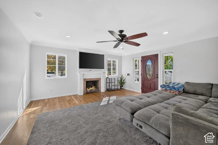 Living space featuring wood-finish flooring, a fireplace with a decorative mantel, recessed lighting, and a ceiling fan