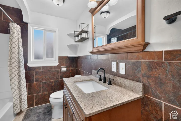 Bathroom vanity featuring a stone-composite countertop, undermount sink, and matte black widespread faucet, complemented by full-height tile wall surrounds and a built-in wood-frame mirror