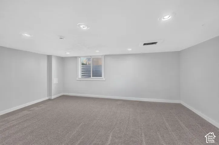 Neutral-toned interior space featuring recessed ceiling lighting, wall-to-wall carpeting, and a single window with a horizontal sliding pane