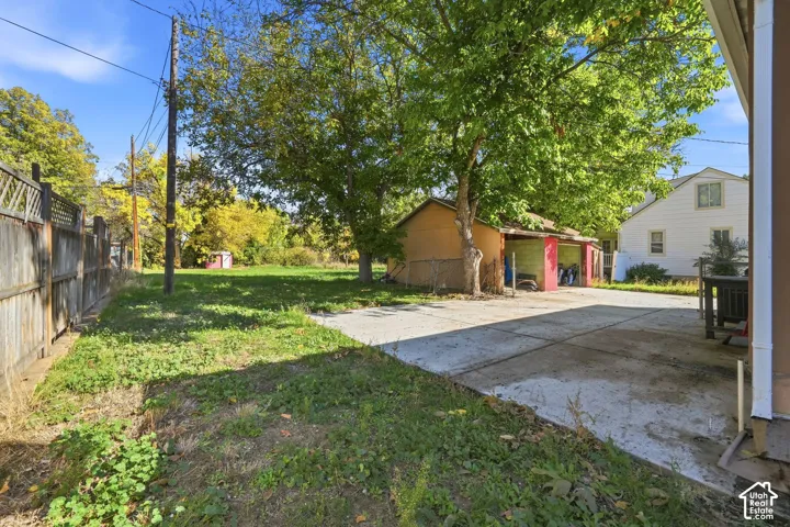Large outdoor area featuring a concrete driveway, detached garage, mature trees, and wood fencing