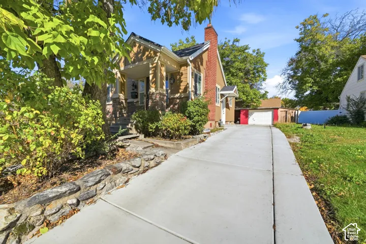 Exterior elevation featuring a covered front porch, stone foundation detailing, an external red-brick chimney, and an expansive concrete driveway leading to a detached garage