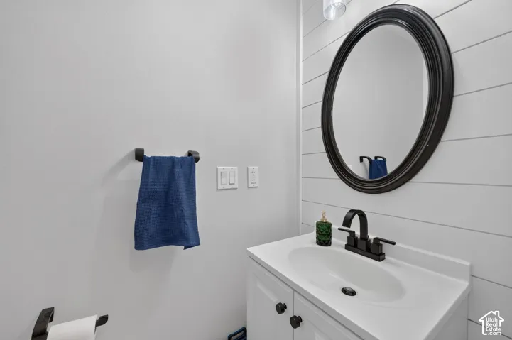 Vanity with an integrated sink, white shiplap accent wall, oval mirror with a dark frame, and matte black plumbing fixtures