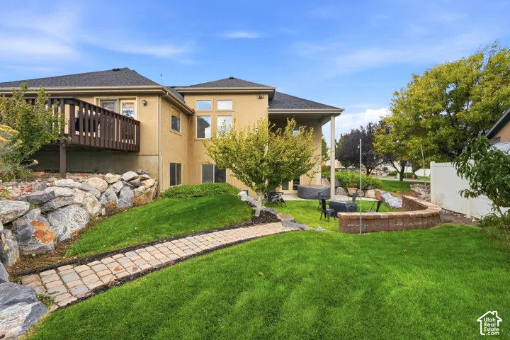 Backyard featuring a tiered stone retaining wall, paved stone walkway, elevated wood-finish deck, and custom brick masonry planter