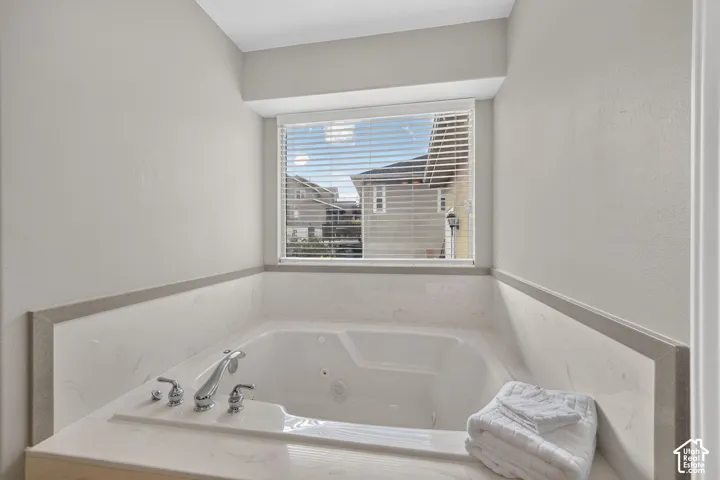 Jetted soaking tub with chrome hardware, set within a neutral-toned tile surround and topped with a deep window sill