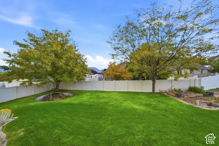 Backyard featuring a manicured lawn, white vinyl fencing, mature trees, and tiered garden beds