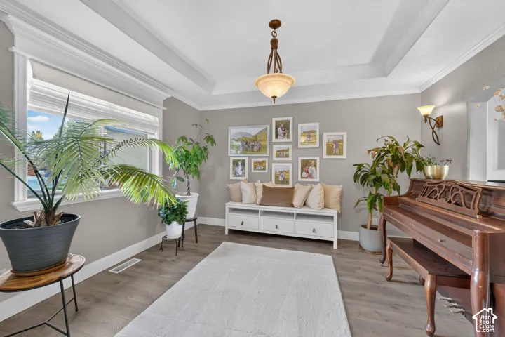 Tray ceiling with crown molding, wood-finish flooring, central pendant light fixture, and wall-mounted sconce lighting