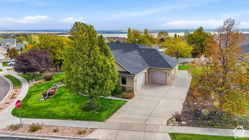 Single-story residence featuring a multi-car garage, stone and stucco exterior, asphalt shingle roof, concrete driveway, and landscaped corner lot