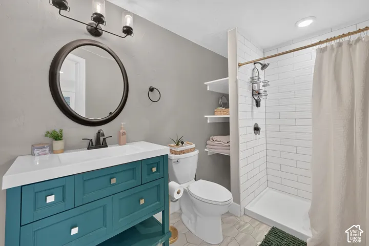 Teal vanity featuring a white countertop and rectangular undermount sink, circular wall mirror, matte black fixtures, built-in shelving, and white subway tile shower surround