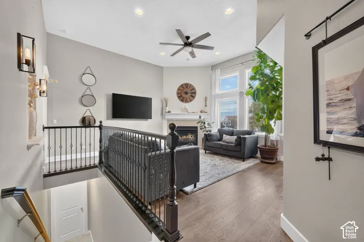 Living area featuring tall windows, a fireplace with a mantel, recessed ceiling lighting, a ceiling fan, and metal baluster railing