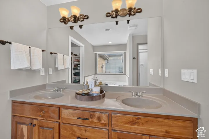 Dual-sink vanity featuring stained wood cabinetry, solid-surface countertops, integrated dual basins, and wall-mounted multi-light fixtures