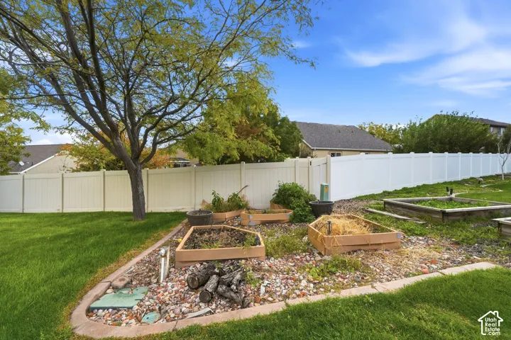 Backyard featuring raised garden beds, gravel ground cover, a manicured lawn, and perimeter white vinyl fencing