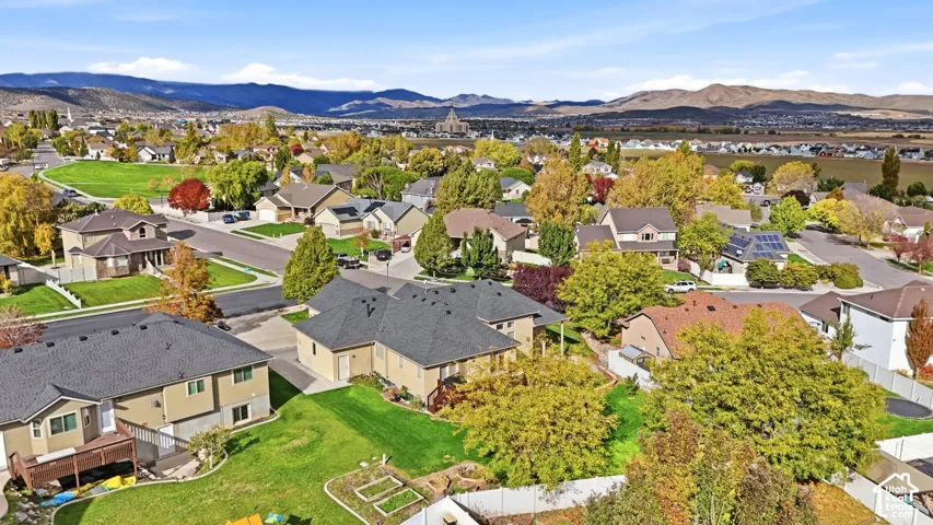 Aerial perspective of residential property featuring a manicured lawn, established deciduous trees, and a mountain backdrop