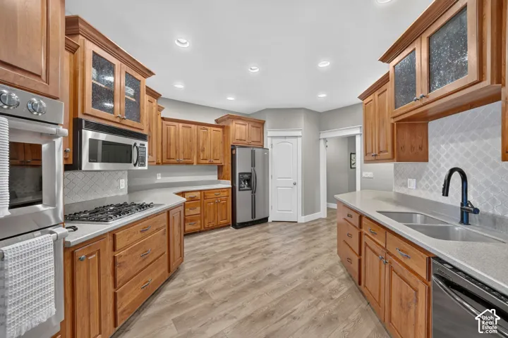 Kitchen featuring natural wood cabinetry, stainless steel appliances, solid-surface countertops, diamond-pattern tile backsplash, and wood-finish flooring