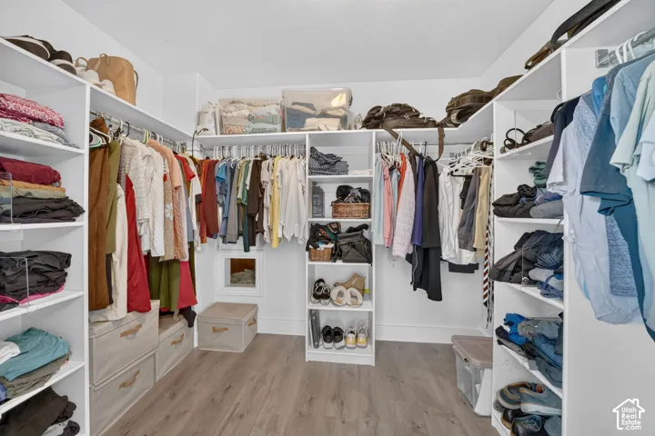 Walk-in closet featuring white built-in shelving, hanging rods, and wood-finish flooring
