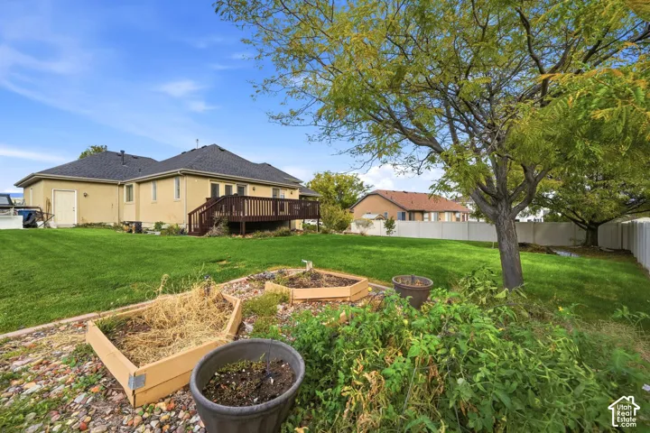 Expansive backyard featuring a manicured lawn, raised garden beds, a wood deck, and perimeter vinyl fencing