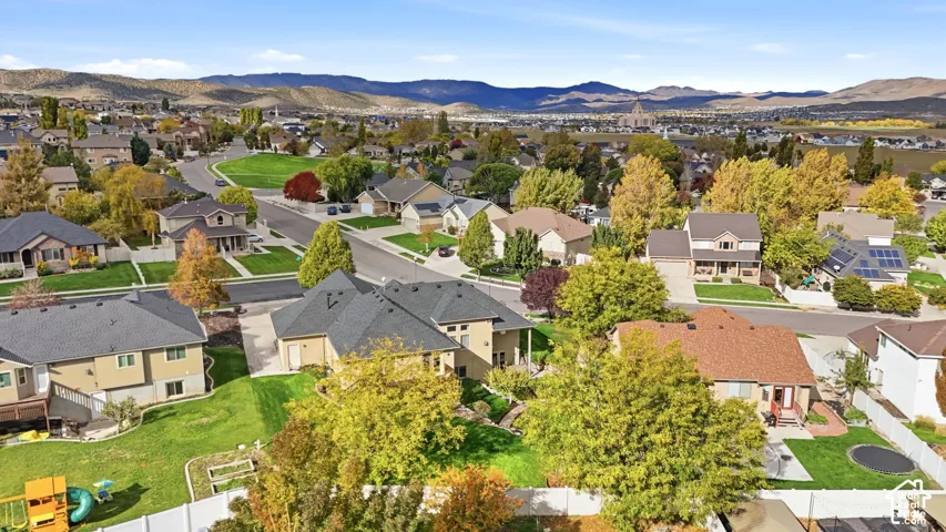 Aerial perspective of a suburban neighborhood featuring mature trees, paved streets, manicured lawns, and a distant mountain backdrop
