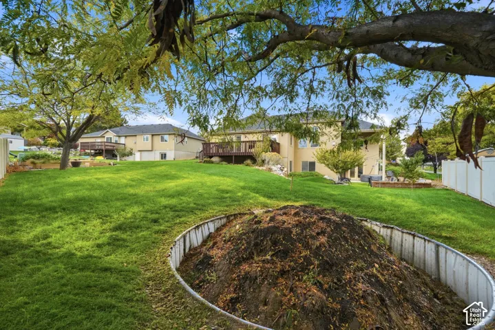Expansive backyard featuring a tiered lawn, mature trees, a raised wood deck, and a circular metal landscape bed