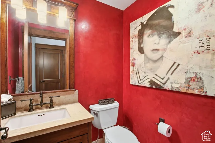 Custom wood vanity with stone countertop, integrated rectangular sink, wall-mounted bronze-finish faucet, and matching framed vanity mirror with integrated multi-bulb lighting