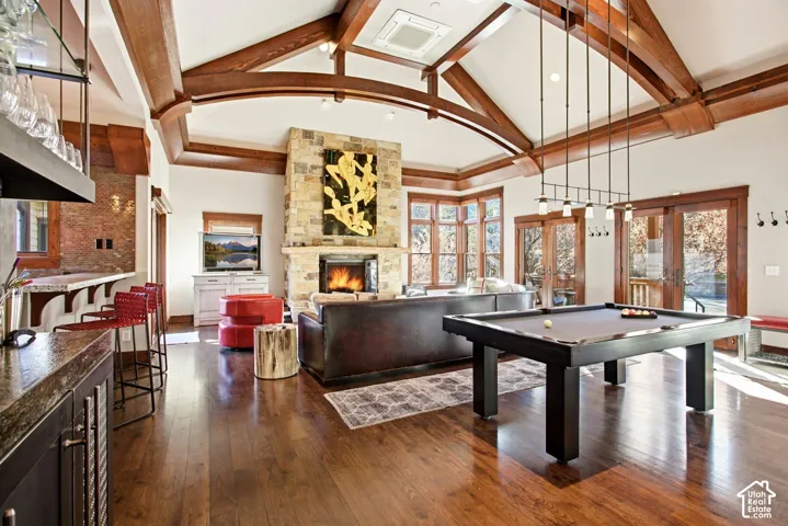 Vaulted ceiling with exposed wood beams, stone-clad fireplace, wood-finish flooring, and built-in wet bar with stone backsplash