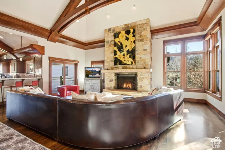 Vaulted ceilings with exposed timber beams, floor-to-ceiling stone masonry fireplace, wood-finish flooring, and expansive windows with natural light
